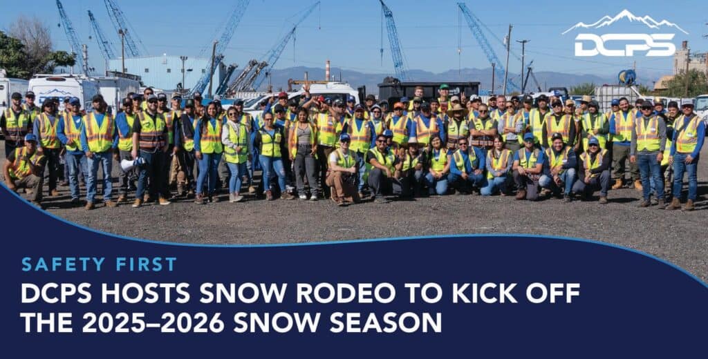 A large group of construction workers in safety vests pose outdoors at a worksite with cranes. Banner reads, "DCPS hosts snow rodeo for 2025–2026."