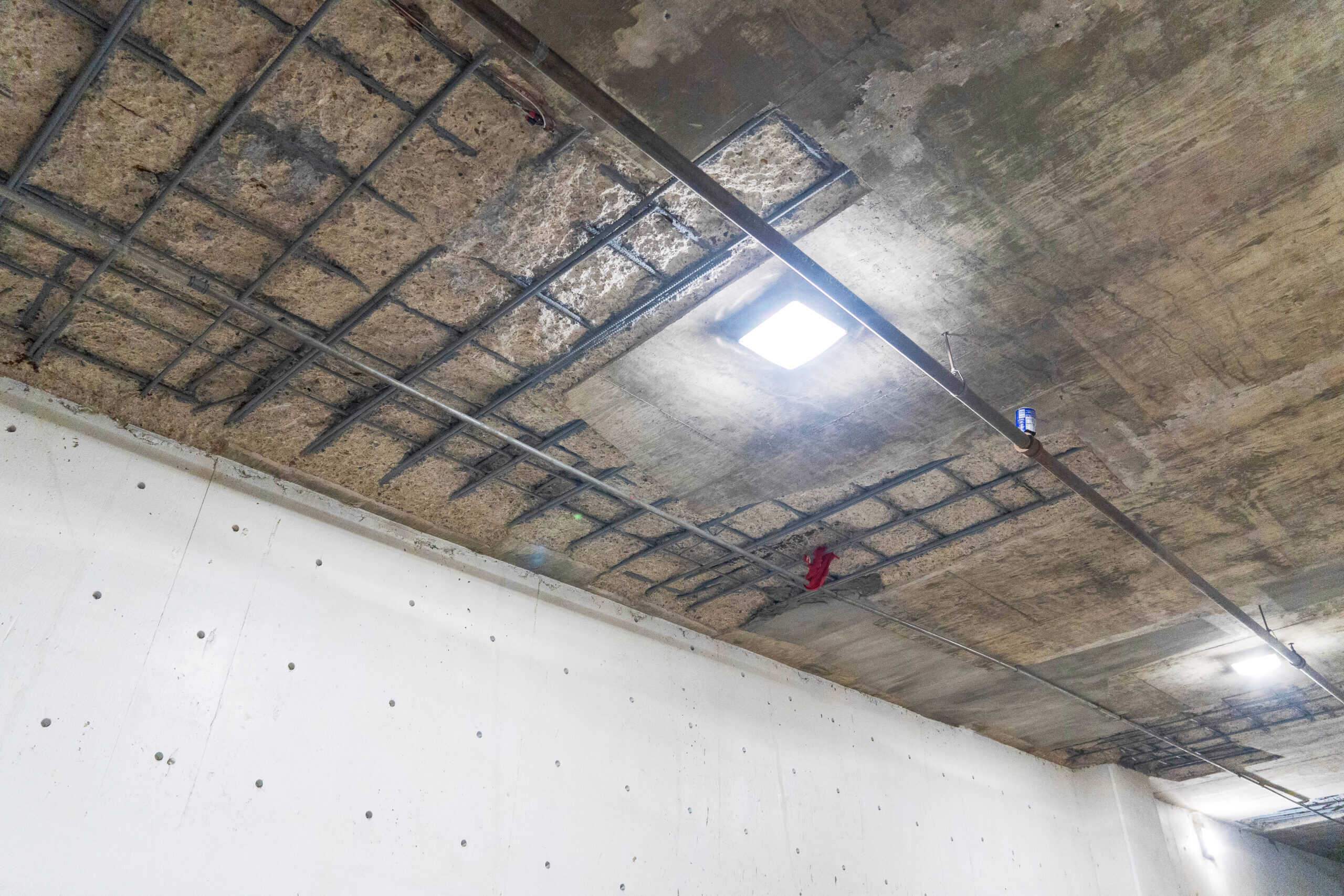 Overhead view of deteriorated concrete ceiling in a parking garage with exposed rebar grid, prior to repair.