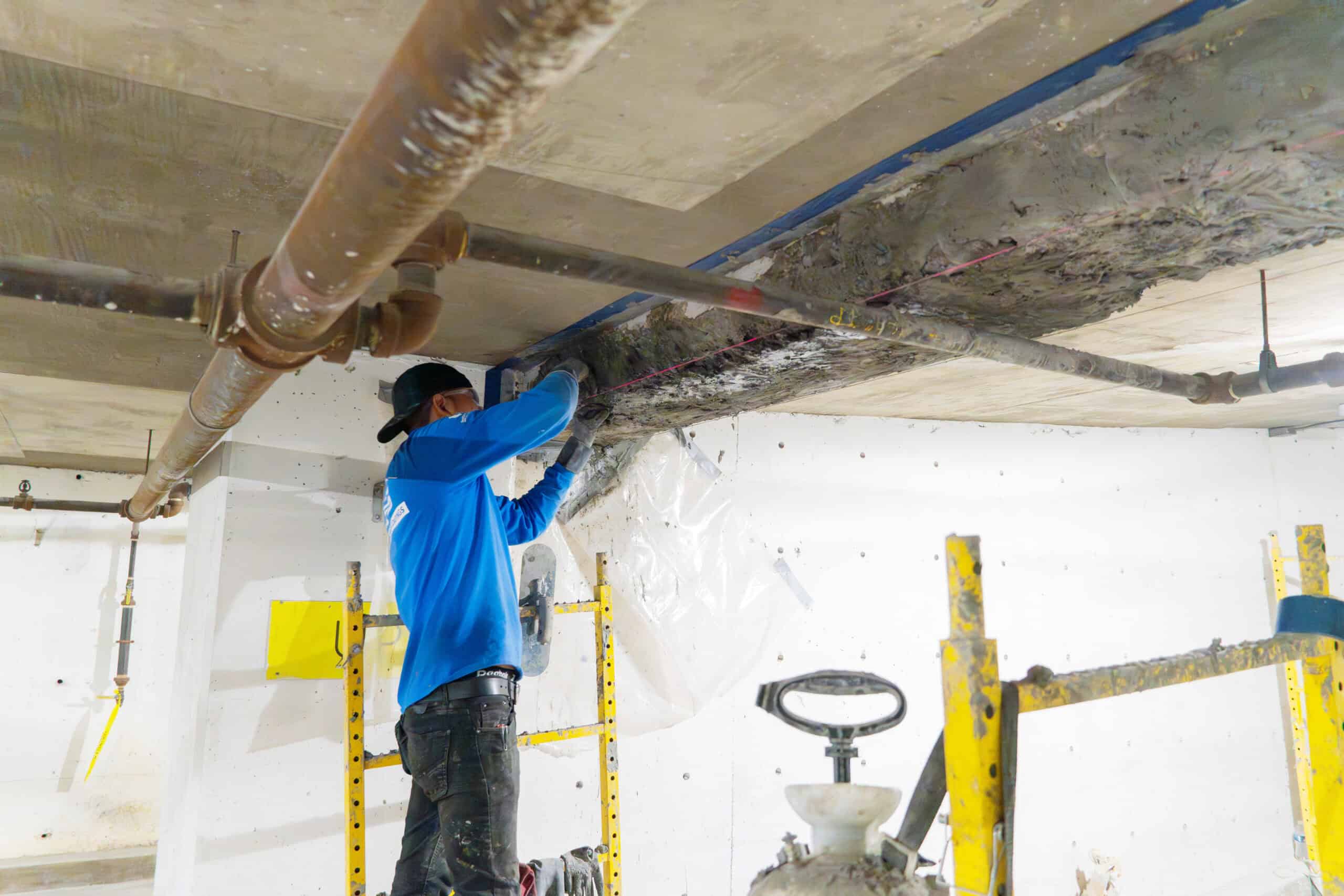 Construction worker applying structural concrete repair overhead to a deteriorated garage ceiling using form and patch techniques.