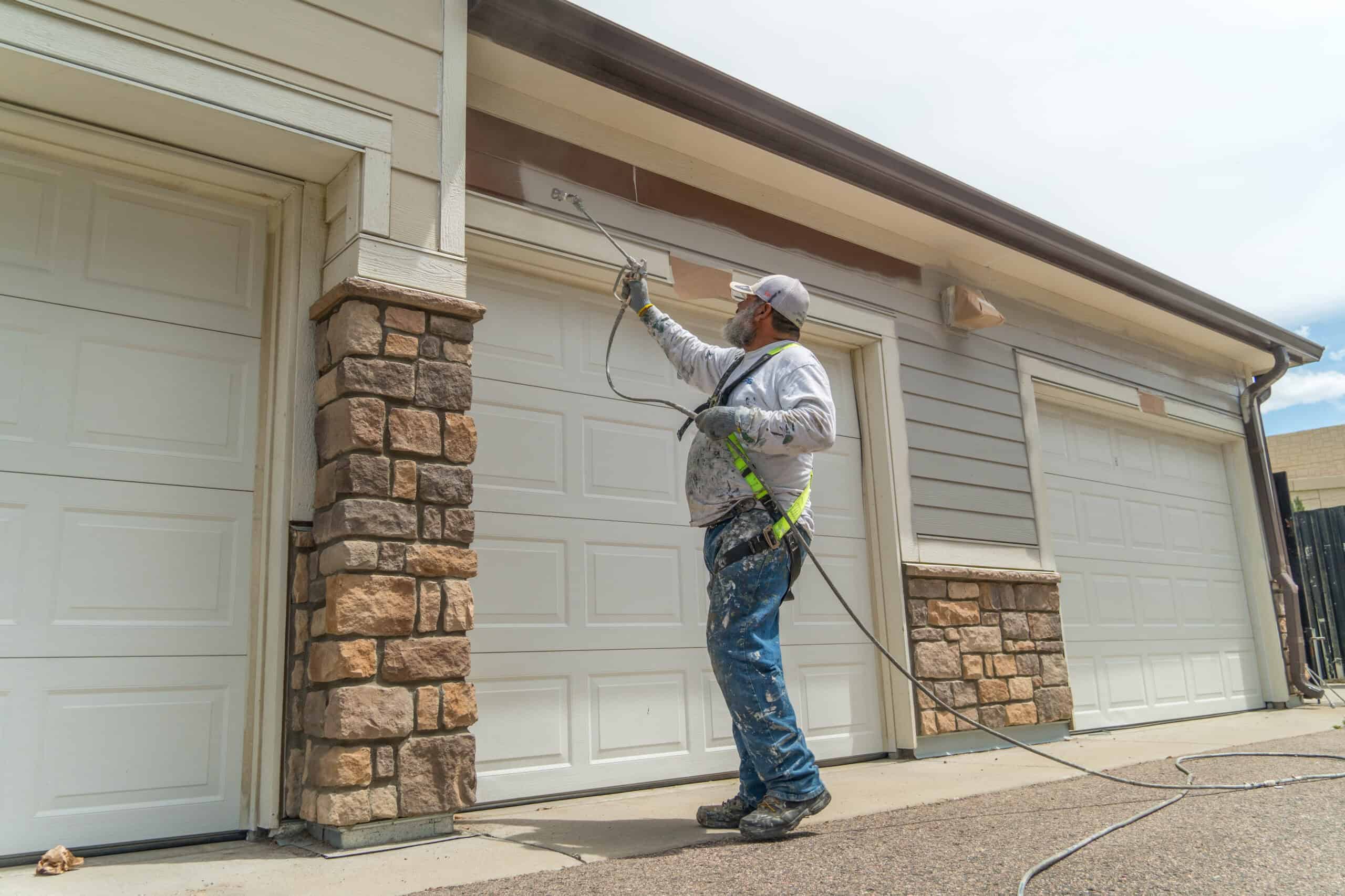 A worker spray painting the exterior of residential garages